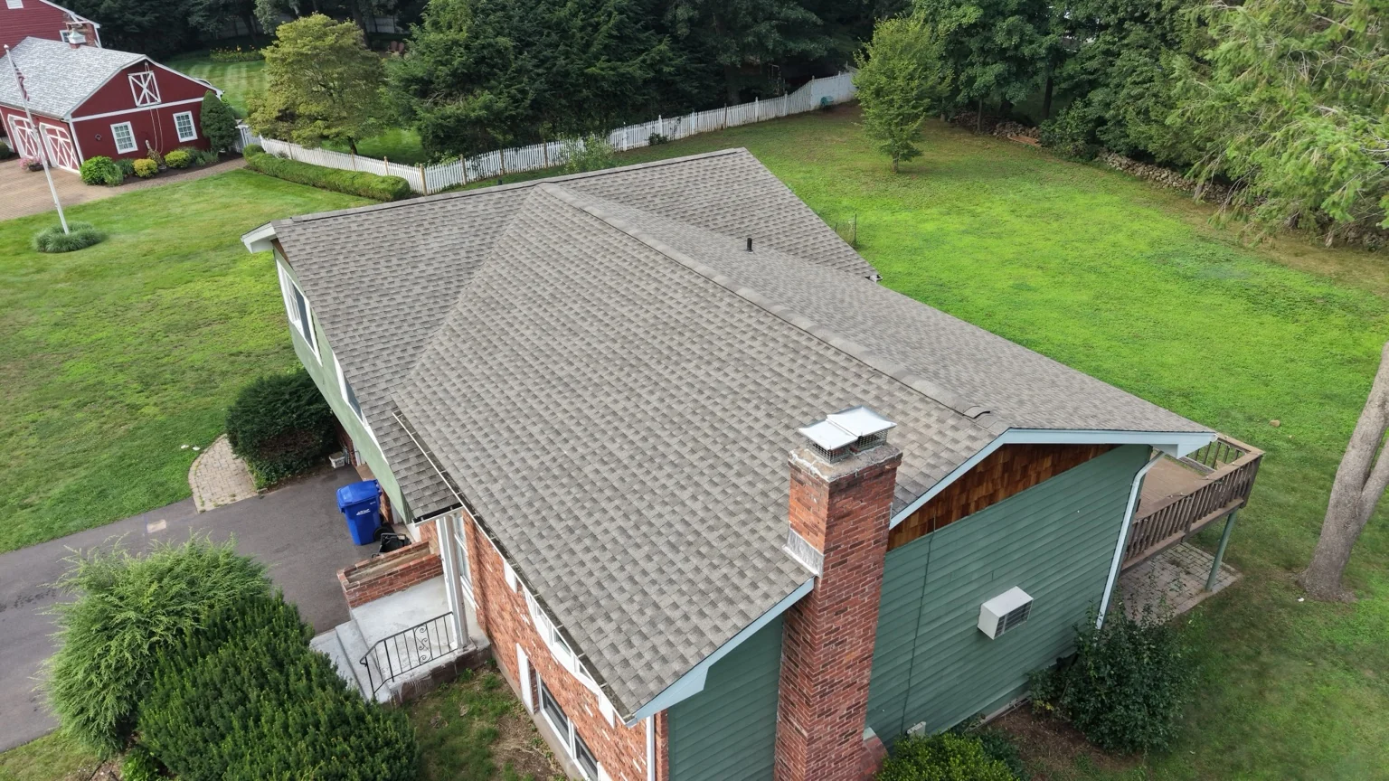 A completed architectural-shingle roof on a green and brick home, with its chimney in view