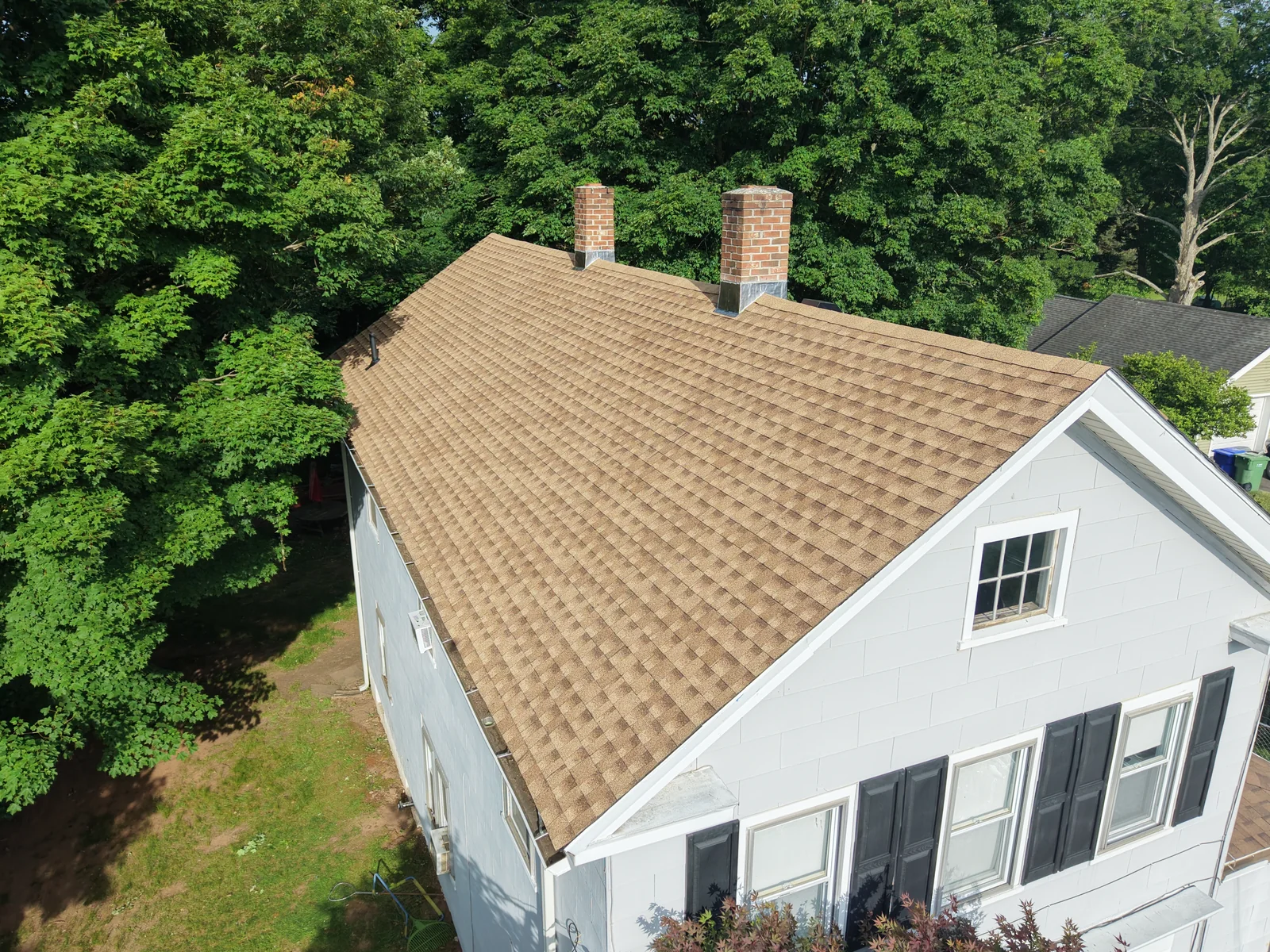 Tan roof shingles on a light-blue house with two brick chimneys